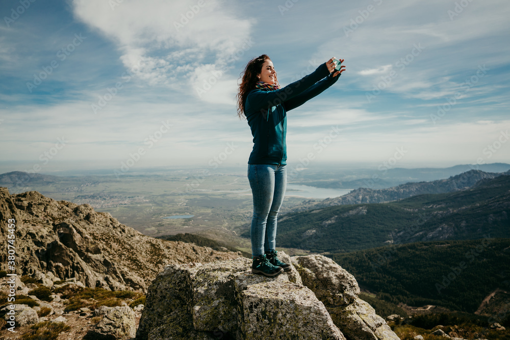 Full body delighted female traveler smiling and taking selfie while exploring Puerto de la Morcuera mountains against cloudy sky in Spain Full body delighted female traveler smiling and taking selfie while exploring Puerto de la Morcuera mountains against cloudy sky in Spain