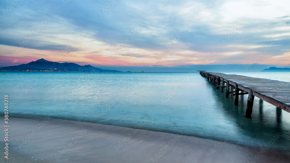 Majestic scenery of wooden quay leading to calm sea water under sunset sky in Playa de Alcudia in long exposure Majestic scenery of wooden quay leading to calm sea water under sunset sky in Playa de Alcudia in long exposure
