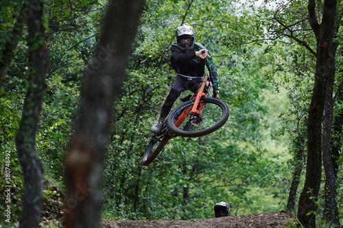 Male cyclists in protective helmets and costumes performing dangerous stunts on bikes for downhill on trail in forest photo