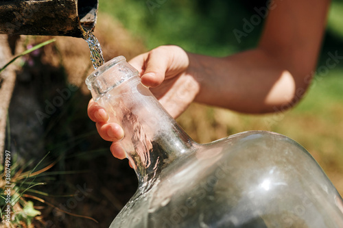 Crop woman filling plastic bottle with fresh water from natural spring in rock in sunny day photo