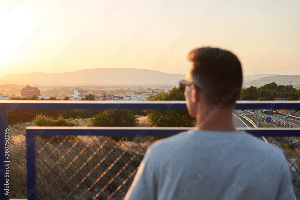 Confident male musician standing with guitar in case on bridge near railing and looking away Confident male musician standing with guitar in case on bridge near railing and looking away