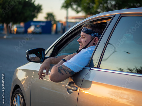 Hombre joven sacando la cabeza por fuera del coche durante su viaje, vistiendo mascarilla © David Martínez