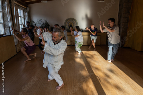 Full body of mature male instructor with group of diverse people performing chi kung pose during practice in studio photo