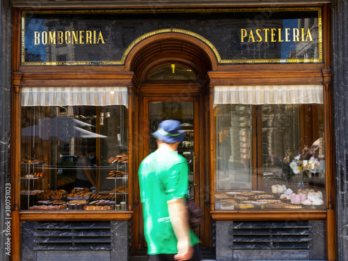 Back view of unrecognizable man walking past showcase with tasty pastry in modern bakehouse located in city