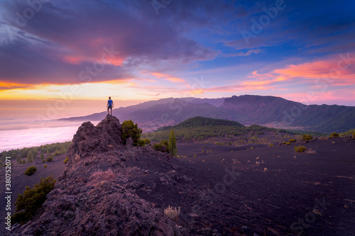 Back view of anonymous male traveler standing with outstretched arms on rocky hill in highlands and enjoying amazing view of clouds