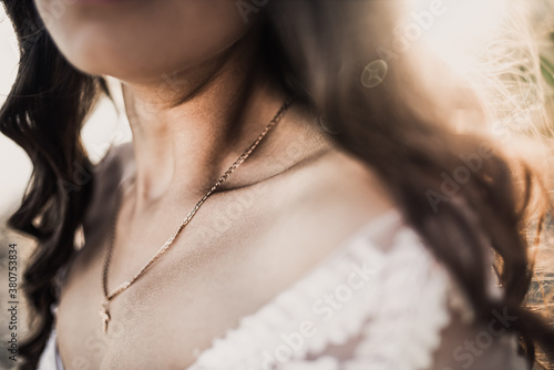 Long haired skinny tanned brunette with curly hair with bare shoulders and a beautifully defined clavicle collarbone in close. bride in a wedding dress on a background of sunbeams