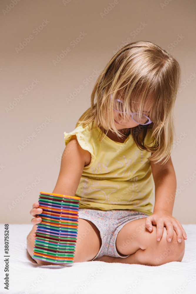 Adorable preschool girl in eyeglasses sitting on floor and playing with colorful educational blocks Adorable preschool girl in eyeglasses sitting on floor and playing with colorful educational blocks