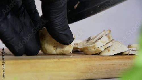 A chef in black gloves is minutely slicing mushrooms with a metal knife on a wooden Board, slow-motion, bright kitchen, close-up 1. photo