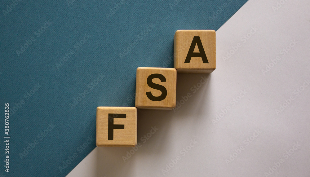 Wood cubes with word 'FSA, flexible spending account' stacking as step stair on paper blue and white background, copy space. Business concept. Wood cubes with word 'FSA, flexible spending account' stacking as step stair on paper blue and white background, copy space. Business concept.