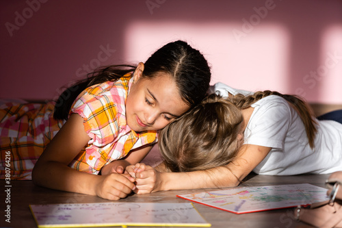 Little girls reading a book in living room. Smart schoolgirls doing their homework after school. Education and distance learning for kids. Homeschooling during quarantine. Stay at home entertainment.