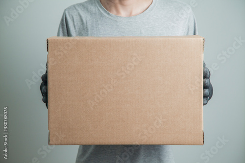 Detail of man with black gloves holding a cardboard box for delivering products on gray background. Delivery concept. Delivery service concept. Copy space. © Gideoni Junior