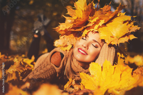 Outdoors lifestyle close up portrait of stunning young woman lying on the grass. Wearing a wreath of autumn leaves. Smiling, walking on the autumn park. Wreath of maple leaves. Autumn colors. Happy