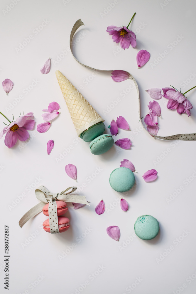 Turquoise and pink macaroons in cone with pink flowers on white background Turquoise and pink macaroons in cone with pink flowers on white background