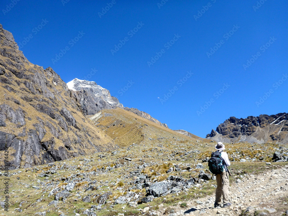 A hiker enjoying a view of the moon low in the morning sky and the mountainous terrain along the Salkantay trek in Peru