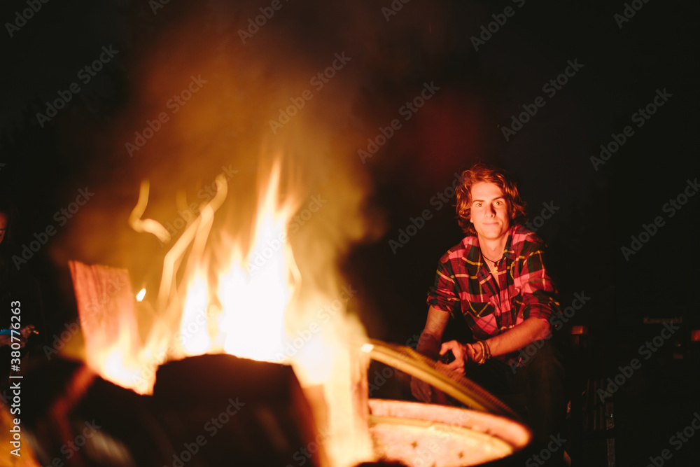 Young boy in flannel sits along side a roaring campfire. Young boy in flannel sits along side a roaring campfire.