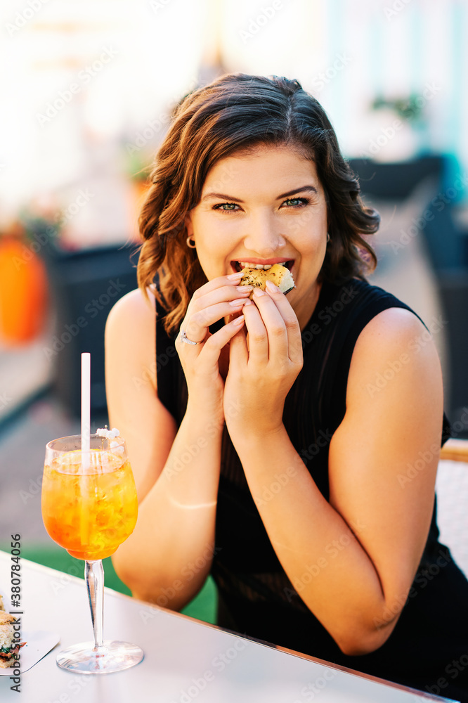 Happy young woman having foccacia snack and iced aperol spritz cocktail after work