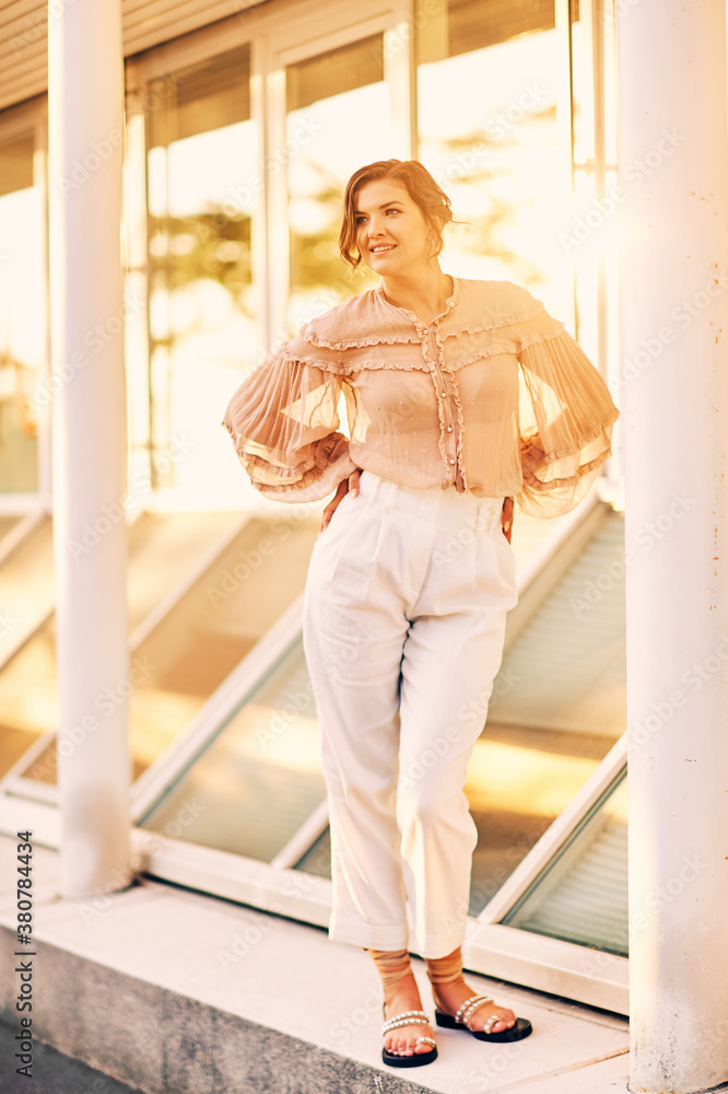 Young stylish woman posing outside in sunset light, wearing beige blouse and white triusers Young stylish woman posing outside in sunset light, wearing beige blouse and white triusers