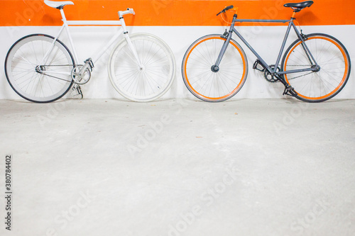 Two fixie bikes with orange line on wall behind. photo