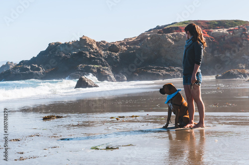 Girl and dog stand on beach lookingout to see photo
