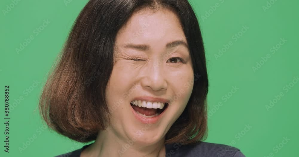 Studio, slow motion, a portrait of a Japanese woman winking against a green screen, London, UK Studio, slow motion, a portrait of a Japanese woman winking against a green screen, London, UK