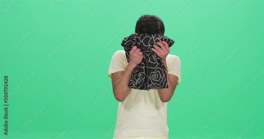 Young Chinese man crying and hiding behind cushion, green screen