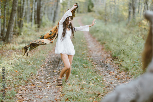 A young girl in a white dress with a scarf is watched by the wolf as she dances around in the woods photo