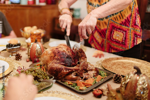 A mother cutting a turkey at the dinner table with family. photo