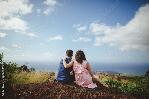 Young couple sitting and cuddling together on hilltop enjoying each other and view photo