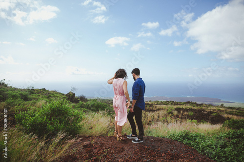 Young, romantic couple standing together outside - wide, scenic view of hills and water photo