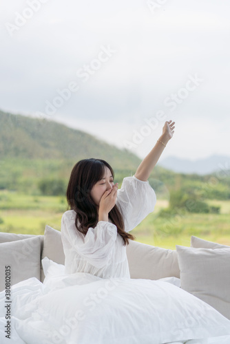 Young long-haired woman in bed is yawning while stretching