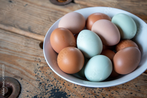 Colorful Fresh Eggs in a white bowl on a wood table