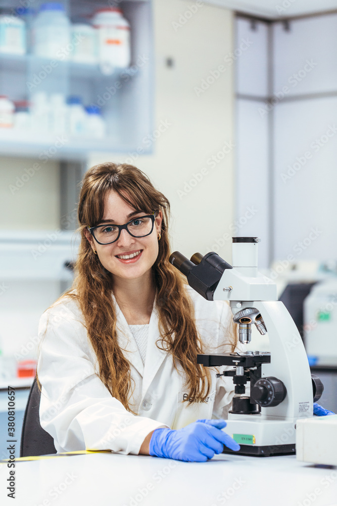 Smiling young biologist in glasses at microscope Smiling young biologist in glasses at microscope
