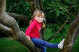 Little toddler girl climbing on tree on family backyard. Lovely happy child hanging on magnolia tree, active games with children outdoors.