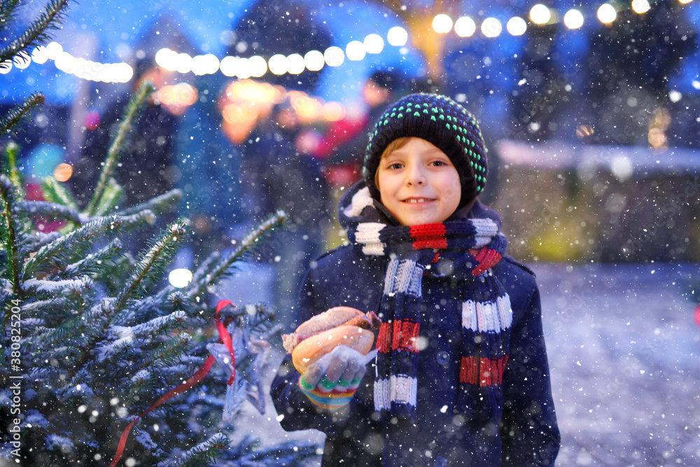 Little cute kid boy eating German sausage and drinking hot children punch on Christmas market. Happy child on traditional family market in Germany. Laughing boy in colorful winter clothes Little cute kid boy eating German sausage and drinking hot children punch on Christmas market. Happy child on traditional family market in Germany. Laughing boy in colorful winter clothes