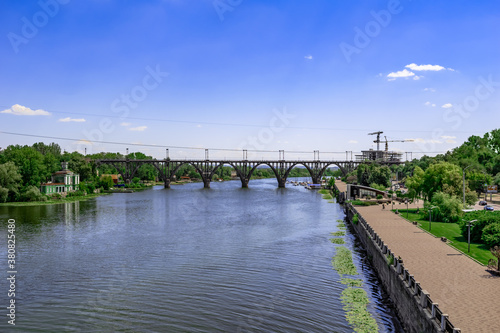 City panorama of Sicheslavska embankment and Merefa-Kherson bridge over the Dnieper river in Dnipropetrovsk (Ukraine). Beautiful cityscape with green trees and blue water surface on a sunny summer day photo