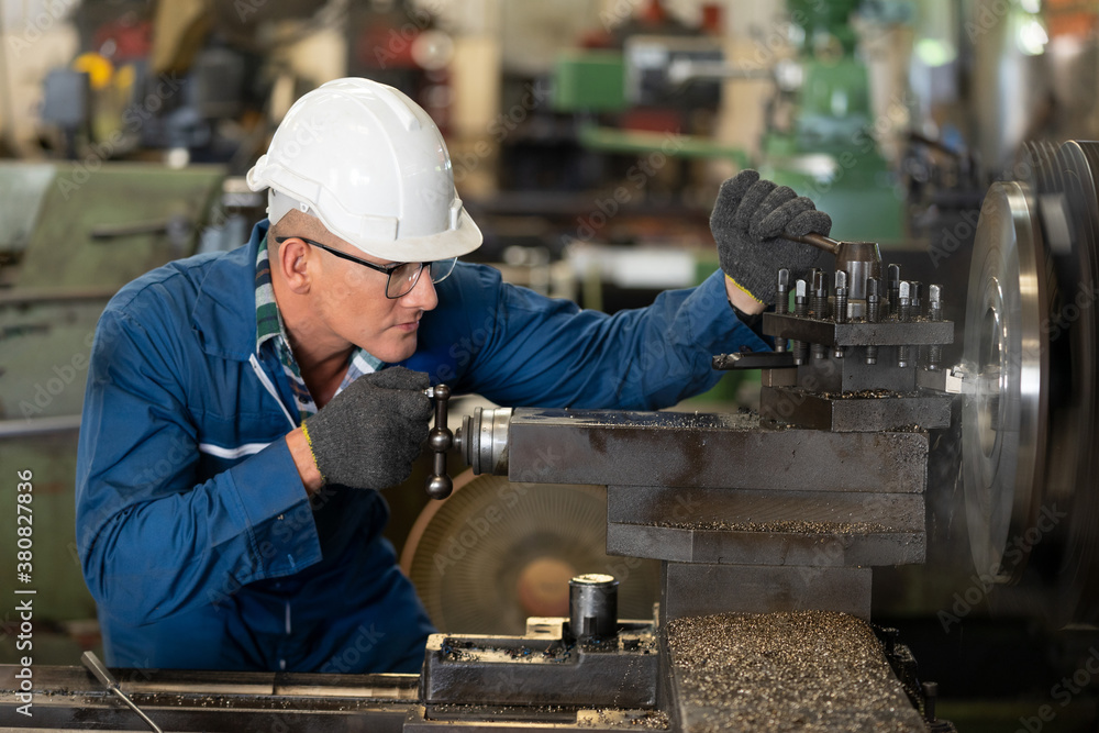 Male worker working on a lathe machine in metal industry factory on a business day. Professional engineer wearing a hard hat and safety glasses operating CNC milling machine in manufacturing workshop. Male worker working on a lathe machine in metal industry factory on a business day. Professional engineer wearing a hard hat and safety glasses operating CNC milling machine in manufacturing workshop.
