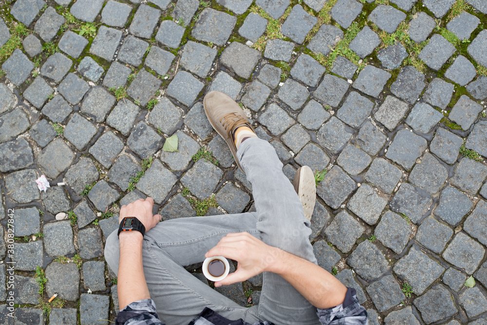 Man sitting and drinking coffee on a cobble stone road Man sitting and drinking coffee on a cobble stone road