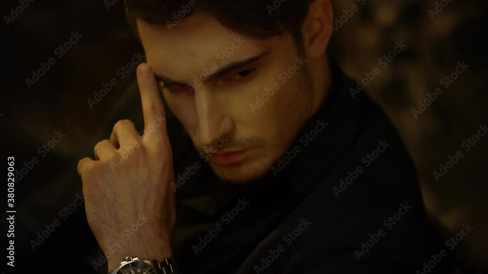 Focused man looking distance in dark background. Rich guy touching face indoors. Focused man looking distance in dark background. Rich guy touching face indoors.