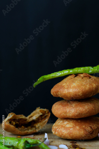 Photography Indian snack kachori served with green chilli and onions in a black background