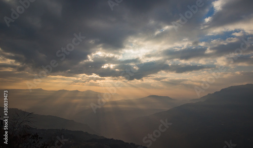 Sun breaking through veil of clouds in himalayan hills.