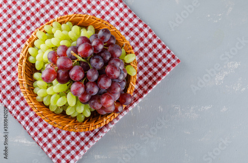 Grapes in a wicker basket on picnic cloth and plaster background, flat lay.