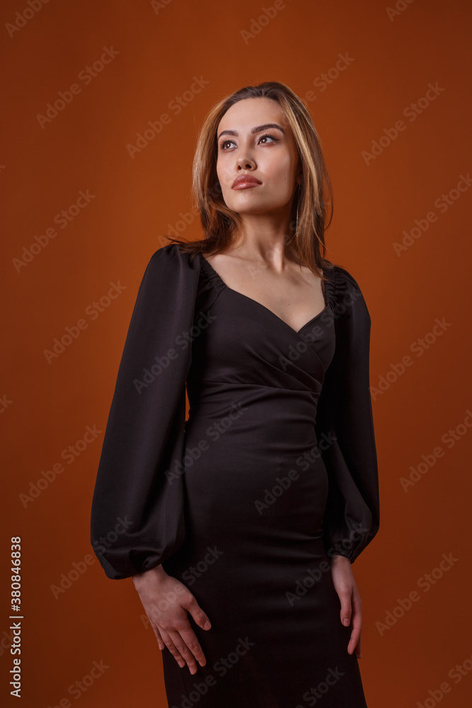 Fototapeta premium charming elegant fashion model wearing black dress with deep neckline posing on orange background. asian skinny young woman in sexy evening gown. beautiful sensual glamorous lady poses in studio