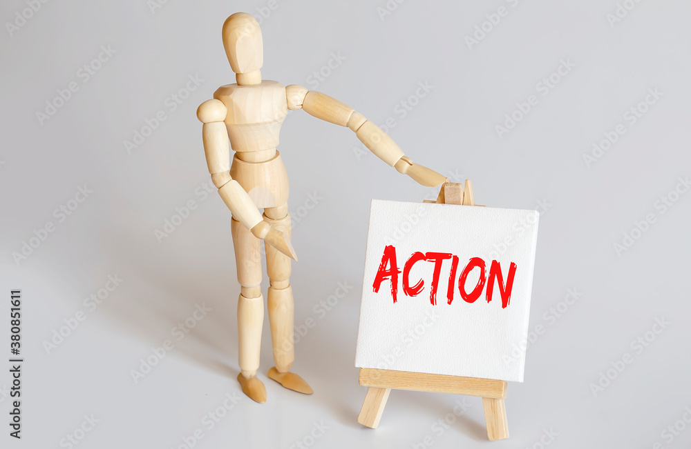 Wooden man shows with a hand to white easel with text ACTION Wooden man shows with a hand to white easel with text ACTION