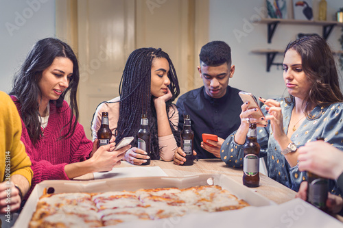 Young people from different races house party. Friends using smartphone drinking beers and eating pizza. Concept of multiracial schoolmates making stuff.