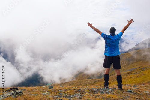A man stands on a mountain with his back to the camera. A man admires the clouds in the mountains. Travel and tourism concept.
