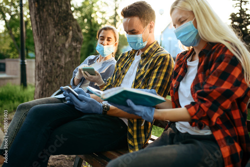 Young people in masks sitting on bench, quarantine