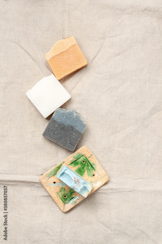 Natural handmade soap bar in ceramic soap dish on linen fabric background