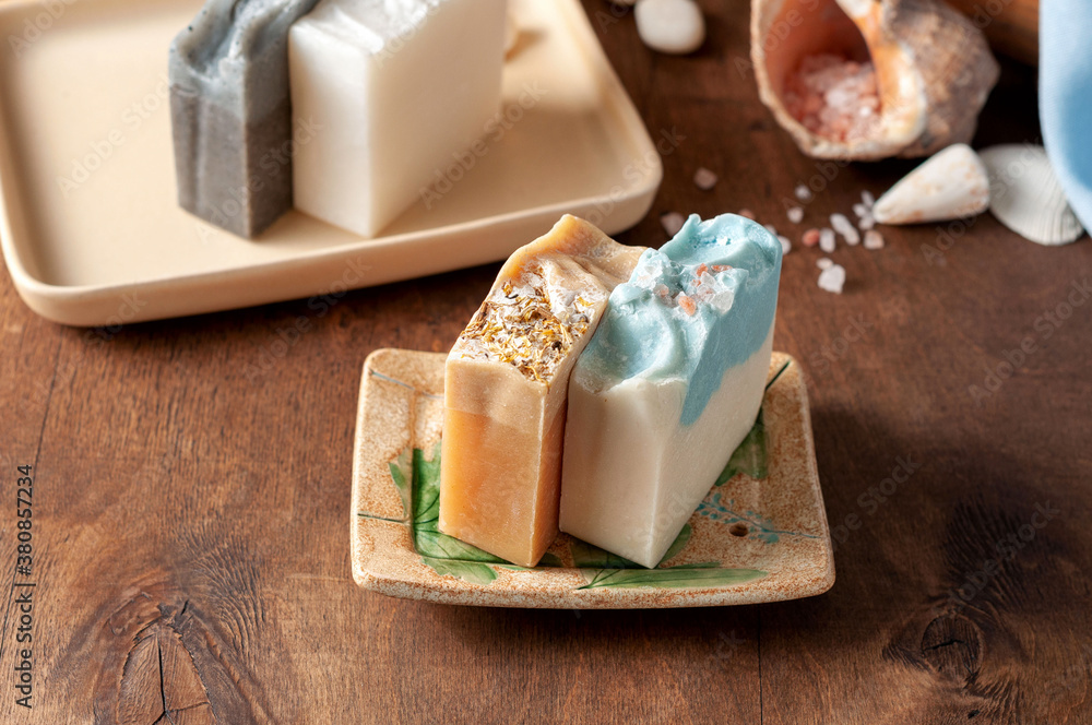 Natural handmade soap bar in ceramic soap dish with spa accessories on wooden table