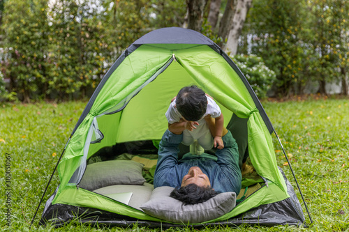 A gay is having a good time with his adopted son in front of tent checking social media with computer laptop
