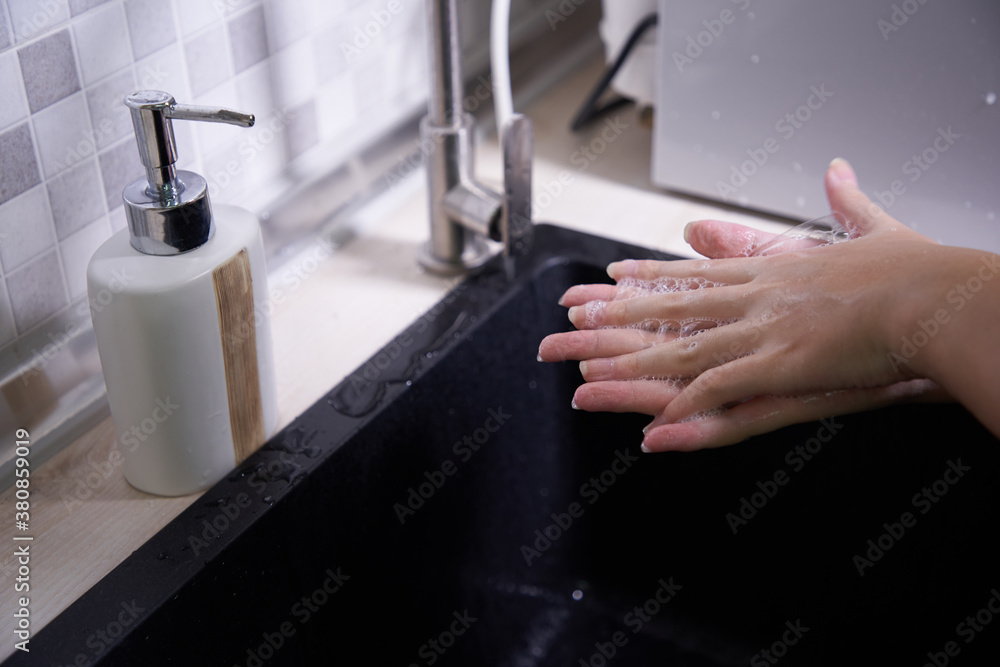 Cropped shot of an unrecognizable woman washing her hands in the kitchen sink at home Cropped shot of an unrecognizable woman washing her hands in the kitchen sink at home